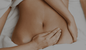 A close-up of a person's torso while another person's hands are massaging their stomach.