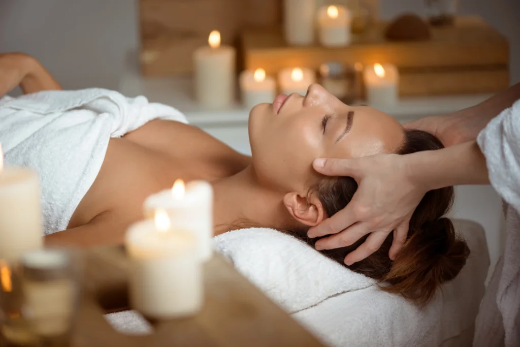 A woman receiving a calming head and scalp massage in a candlelit spa environment.