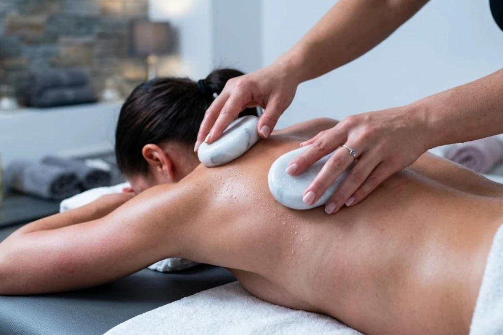 A massage therapist using smooth white marble stones to perform a cold stone massage on a client's back for inflammation relief.