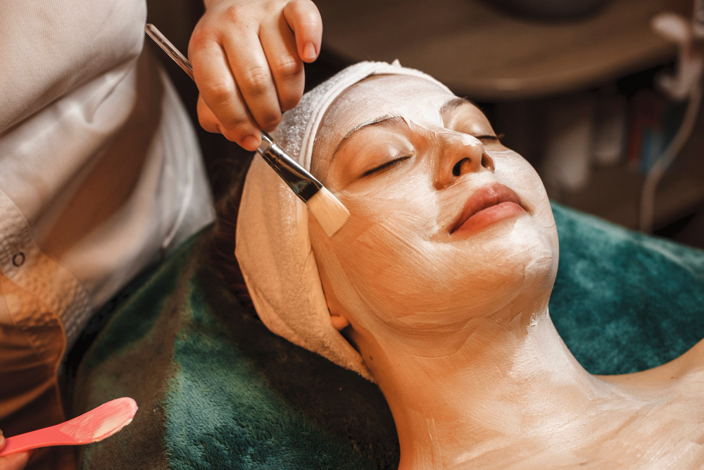 happy-relaxed-woman-leaning-spa-bed-having-skin-care-white-mask-smiling-wellness-spa-center-while-traveling
